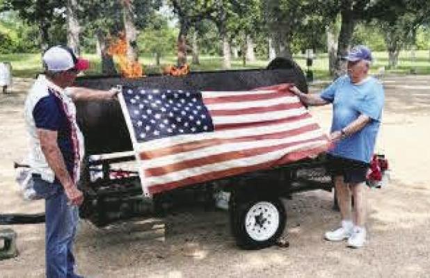 Jim Foster and Jeff Nicholas display an American flag before placing it in the fire for disposal.